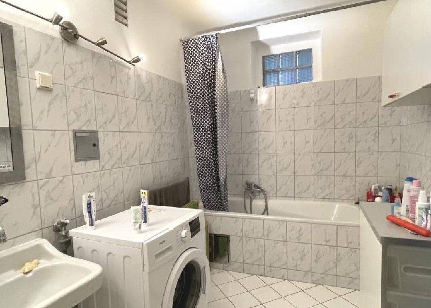 Gefliestes Badezimmer mit Badewanne, Waschbecken und Waschmaschine.