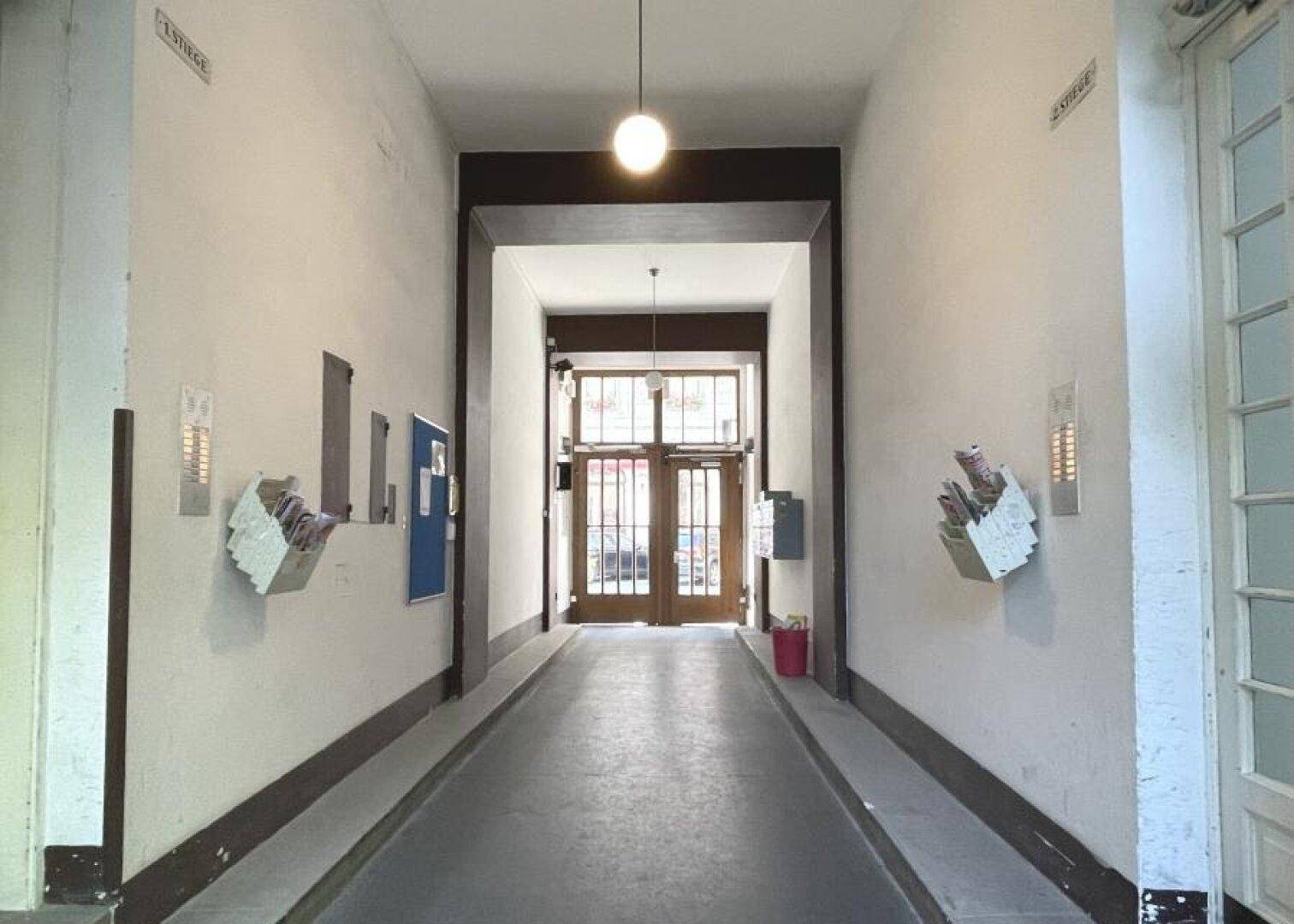 Langer Flur im Eingangsbereich mit hohen Decken und Zugang zum Treppenhaus.