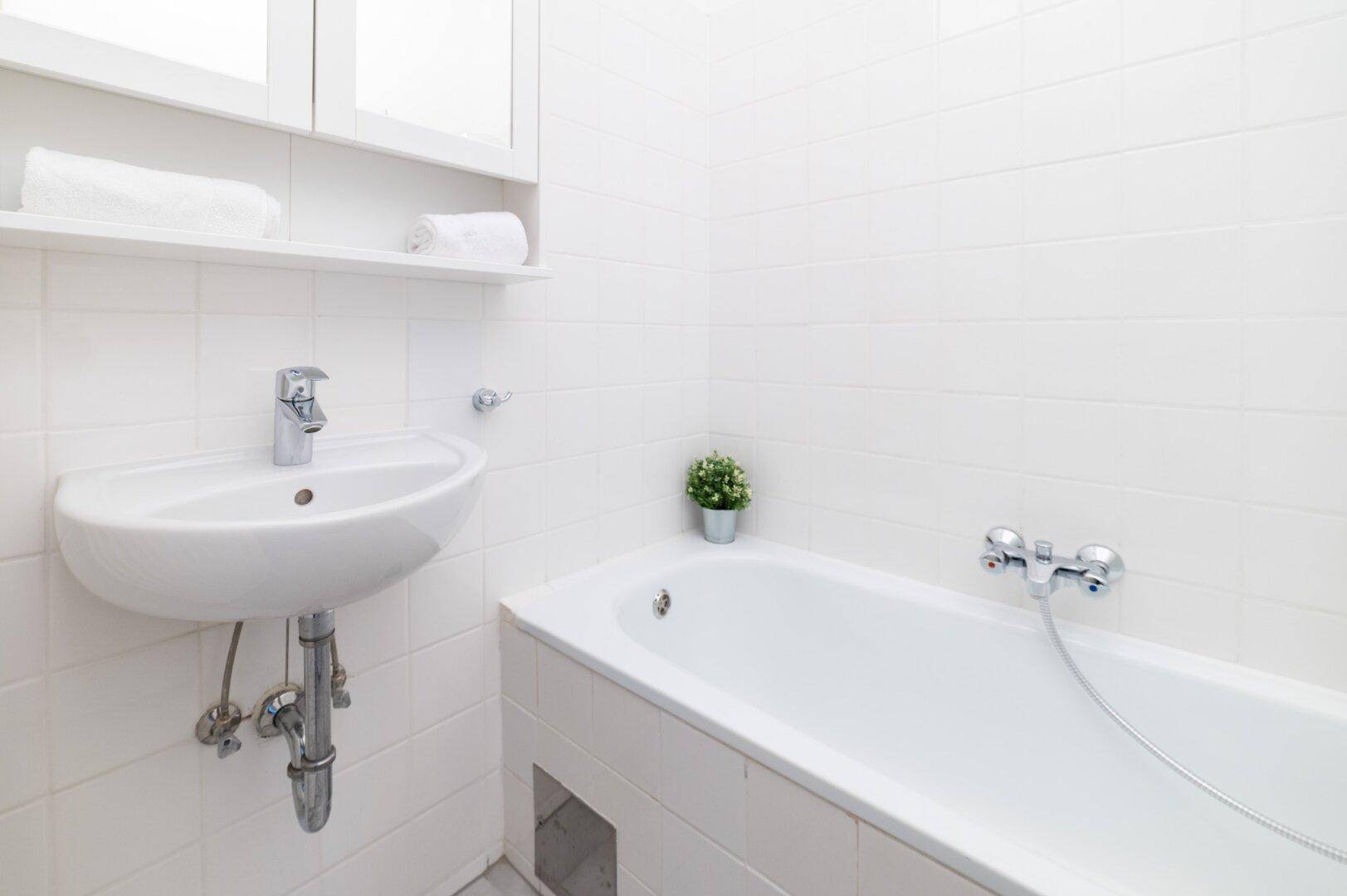 Helles Badezimmer mit weißen Fliesen, Waschbecken und Badewanne.