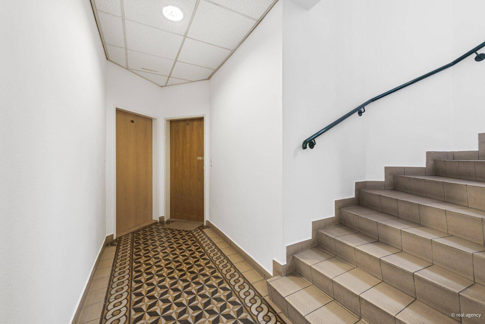 Treppenhaus mit gemusterten Fliesen und Holztreppe, führt zu den oberen Etagen.