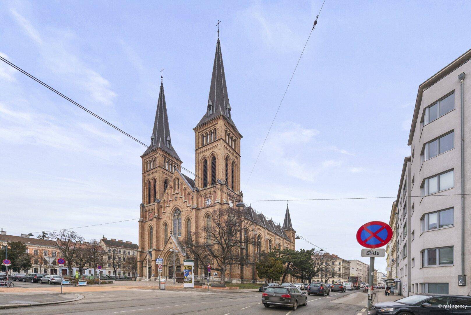 Historische Kirche an einer belebten Straße mit umliegenden Gebäuden und Fahrzeugen.