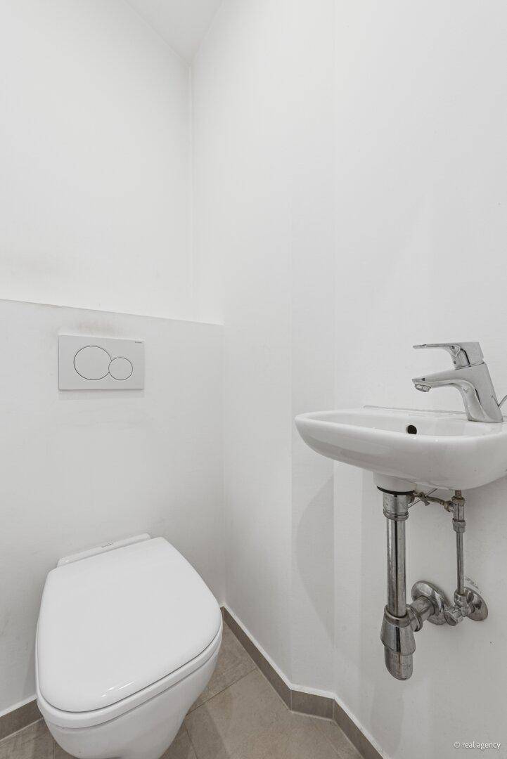 Separates WC mit wandhängender Toilette und kleinem Waschbecken, minimalistisch gestaltet.