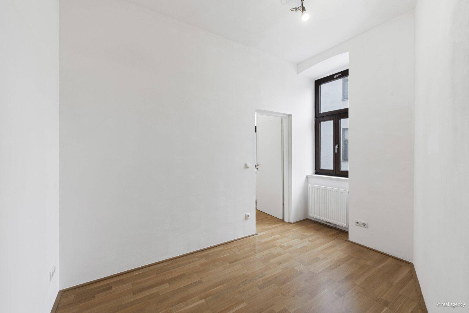 Gemütliches, leeres Zimmer mit Parkettboden und einem Fenster, ideal als Schlaf- oder Arbeitszimmer.
