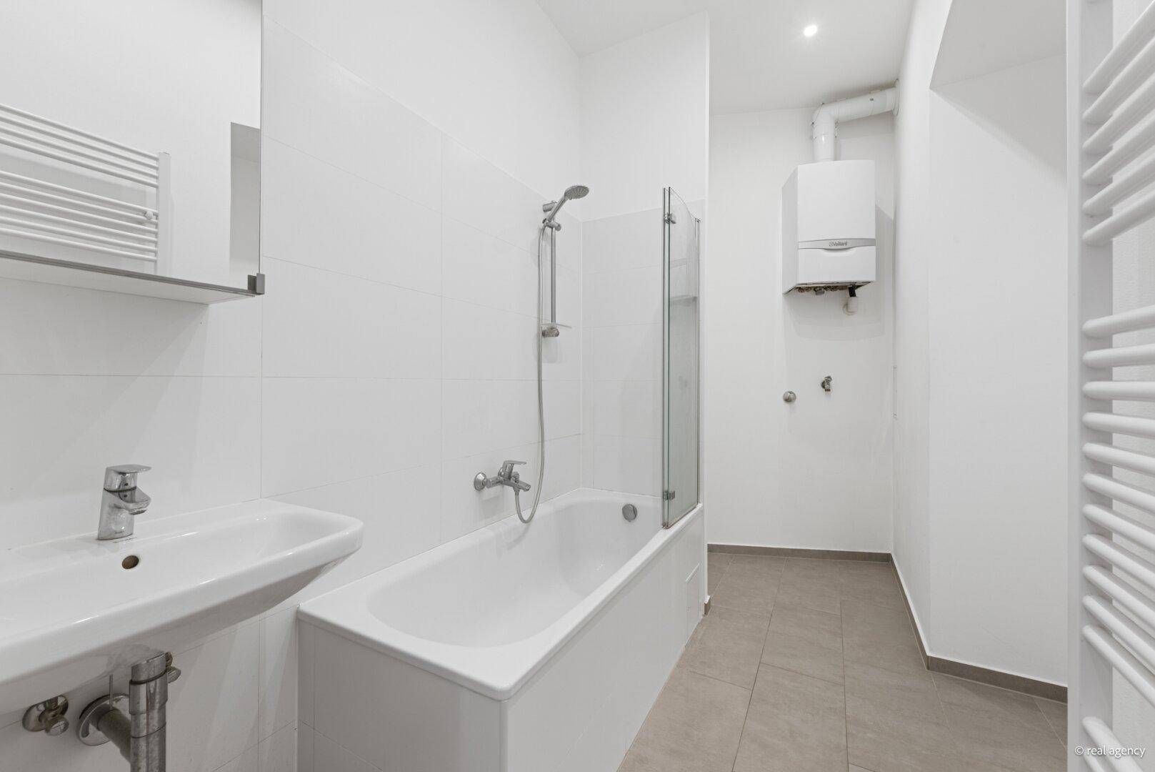 Helles Badezimmer mit Badewanne, Duschabtrennung und Gastherme, funktional eingerichtet.