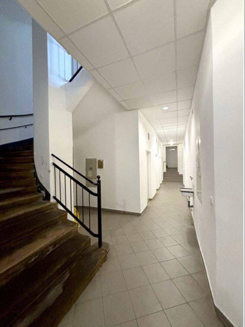 Langer Flur mit Holztreppe, Fliesenboden und weißen Wänden, führt zu weiteren Räumen.