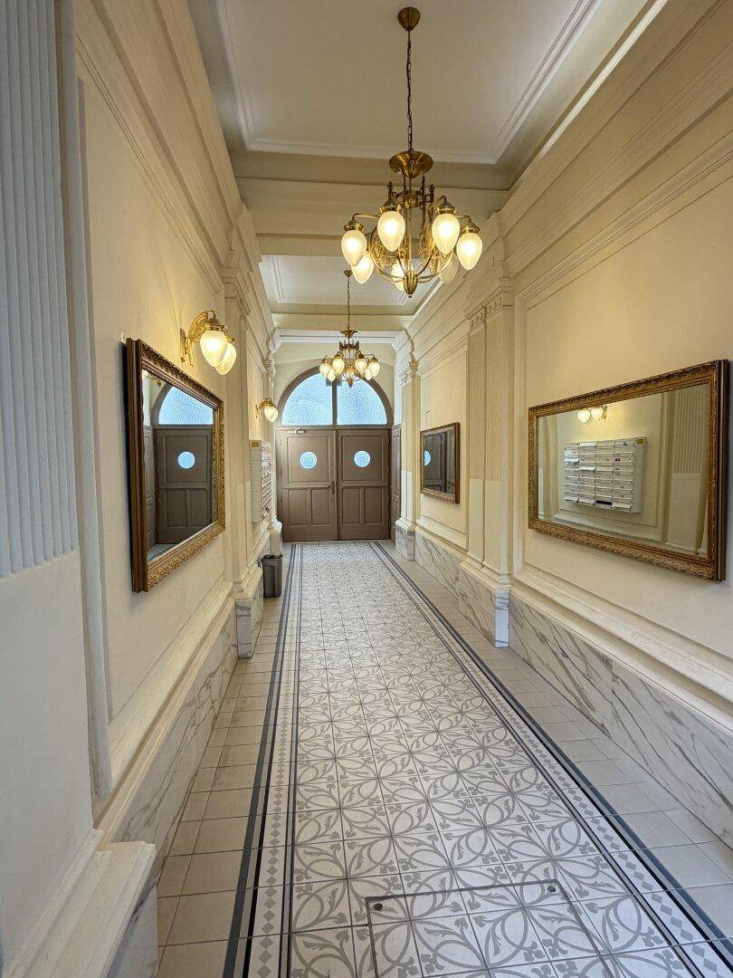 Historischer Hausflur mit kunstvollen Fliesen, Wandspiegeln und eleganten Deckenleuchten.
