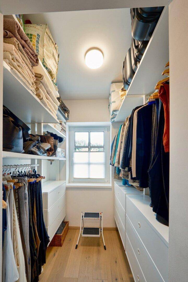 Gut organisierter begehbarer Kleiderschrank mit Regalen, Schubladen und Fenster.