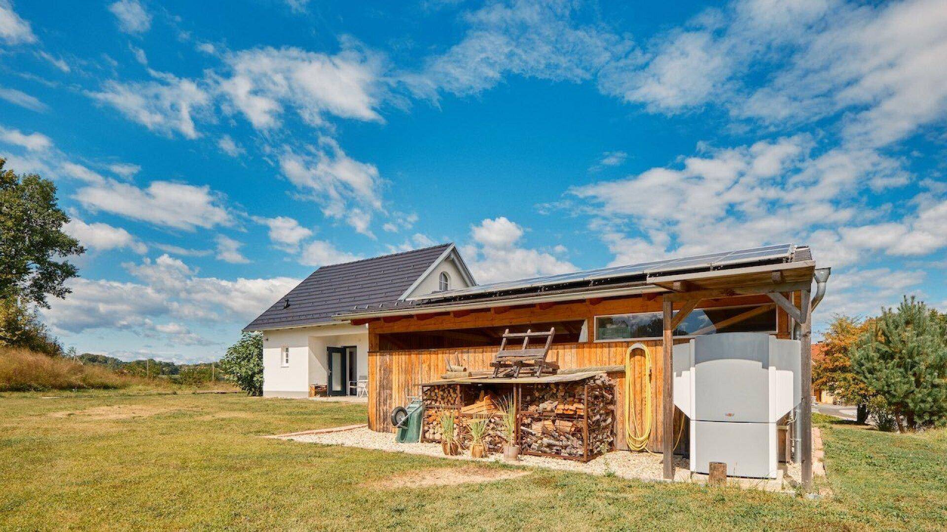 Rustikaler Holzschuppen mit Solarpaneelen auf dem Dach und Brennholzstapel im Garten.