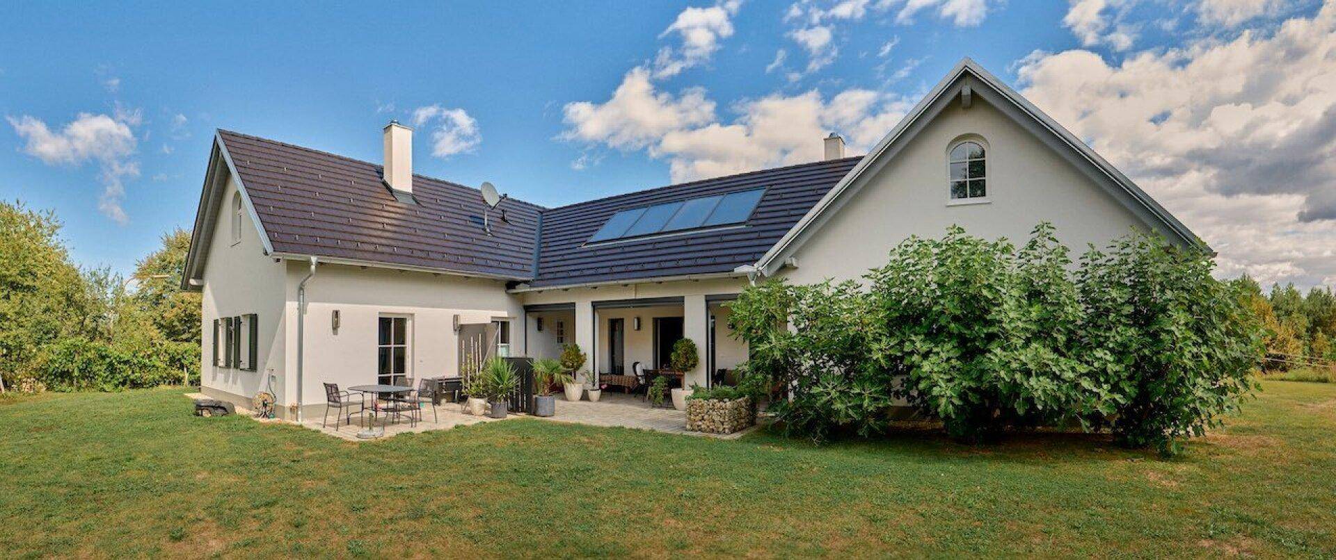 Rückansicht eines modernen Hauses mit großer Rasenfläche, Terrasse und Solarpaneelen auf dem Dach.