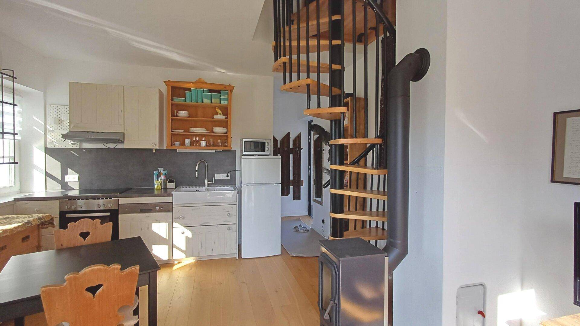 Offene Küche mit Holztreppe, integrierten Geräten und einem kleinen Essbereich.
