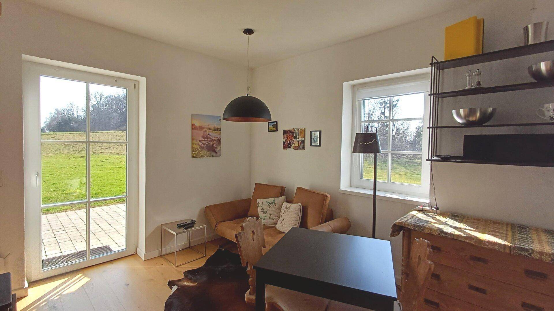 Heller Wohn-Essbereich mit Holzboden, Sofa und Zugang zur Terrasse mit Blick ins Grüne.
