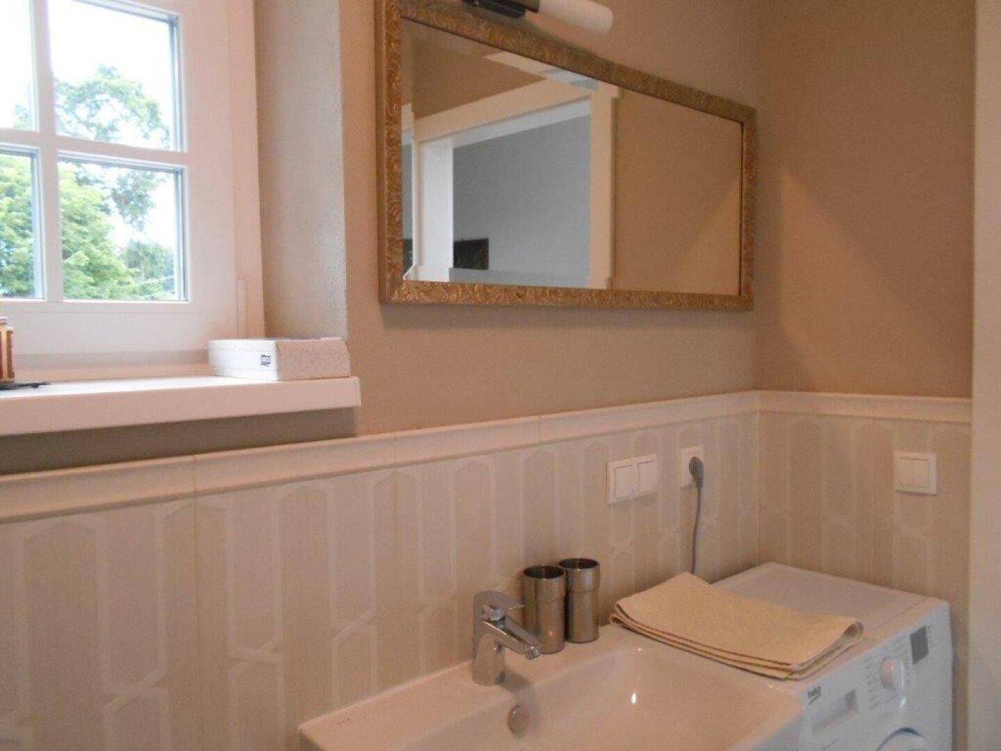 Funktionales Badezimmer mit Waschbecken, Waschmaschine und Fenster für Tageslicht.