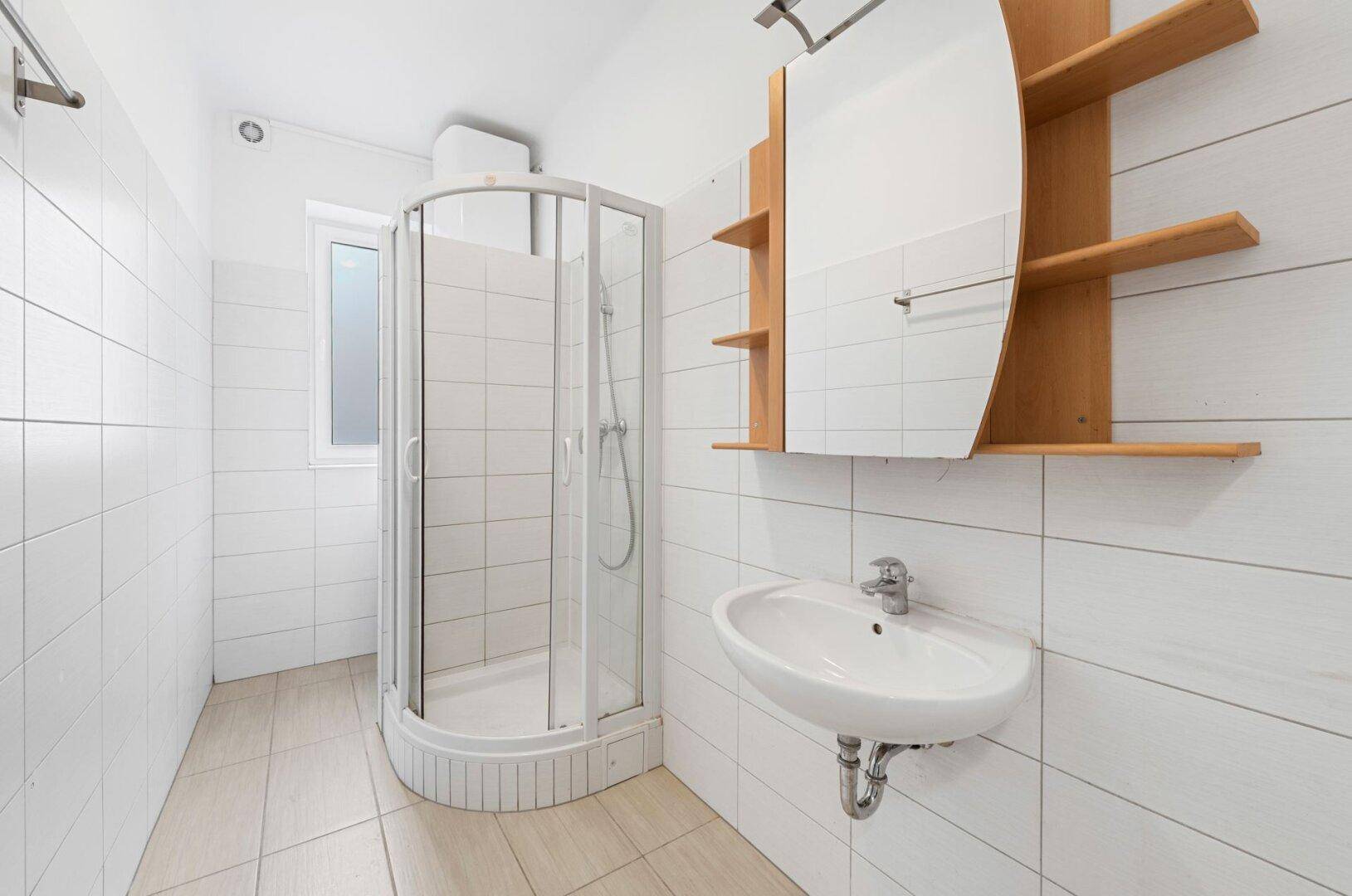 Funktionales Badezimmer mit Duschkabine, Waschbecken und weißen Fliesen.