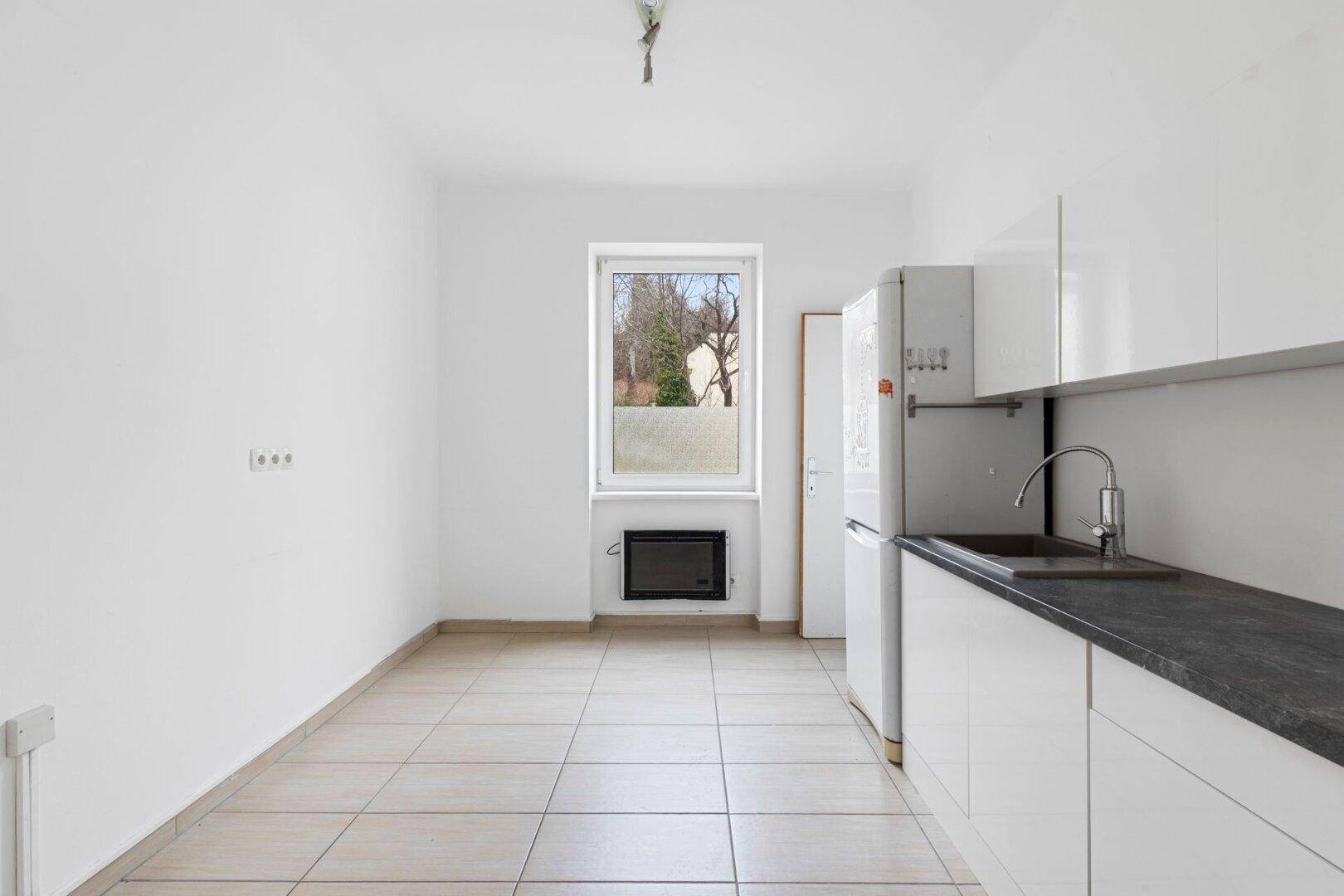 Küche mit Einbauschränken, Spüle, Kühlschrank und Fenster mit Blick ins Grüne.