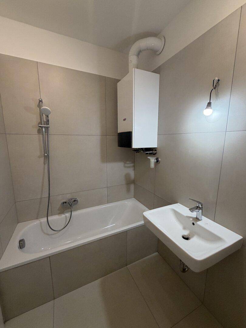 Modern gefliestes Badezimmer mit Badewanne, Duschfunktion und Waschbecken.
