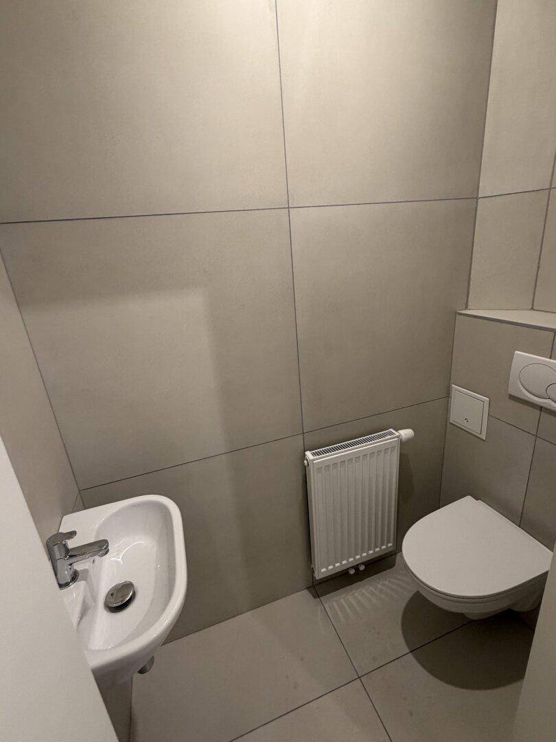 Kleines, modern gefliestes Gäste-WC mit wandhängender Toilette und Waschbecken.