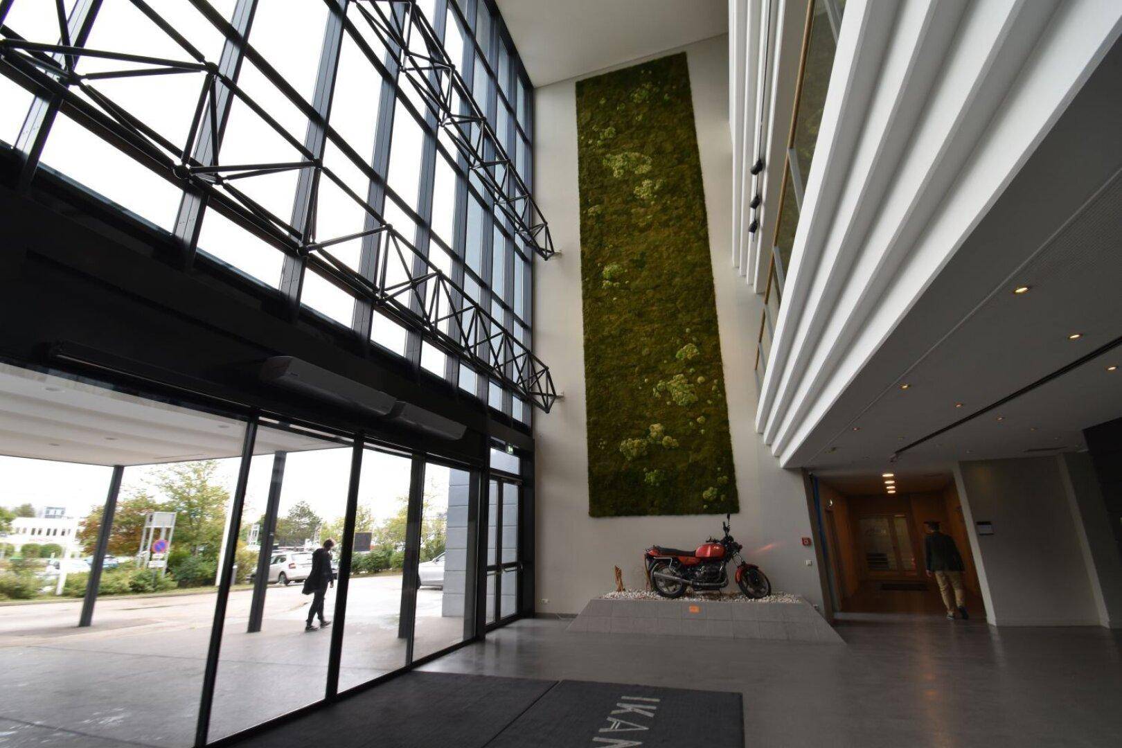 Geräumige und moderne Lobby mit hohen Decken, großen Glasfronten und einer vertikalen Mooswand.