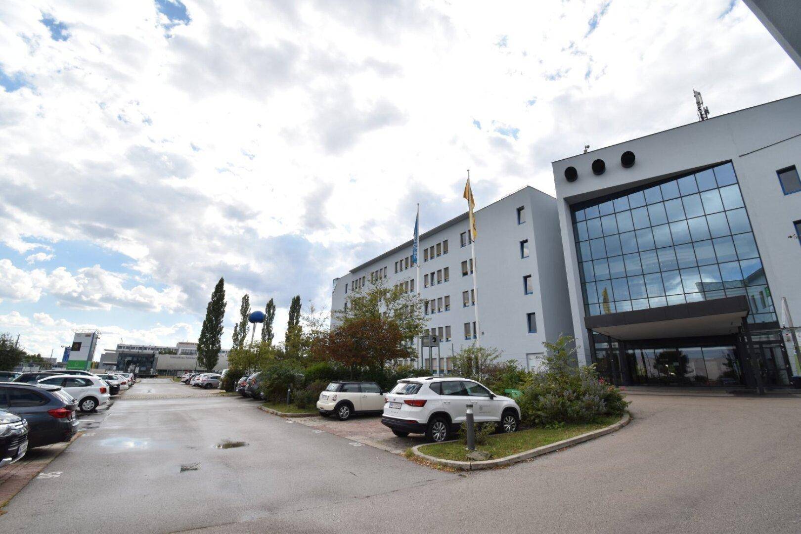 Außenansicht eines modernen Bürogebäudes mit großzügigem Parkplatzbereich unter bewölktem Himmel.