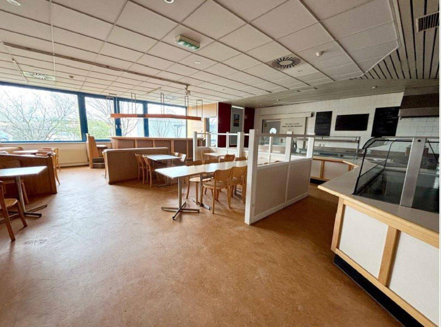 Weitläufiger Restaurantbereich mit großen Fenstern, verschiedenen Sitzgelegenheiten und einem Thekenbereich.
