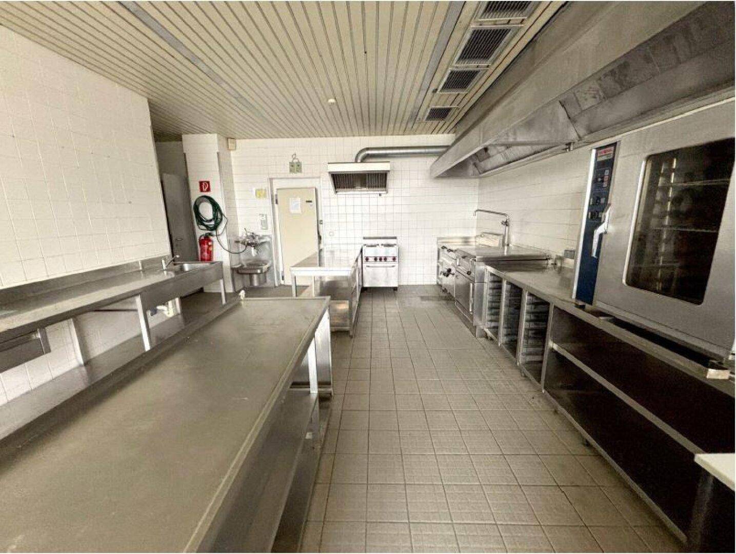 Geräumige und funktionale Großküche mit umfangreichen Edelstahl-Arbeitsflächen und professionellen Geräten.