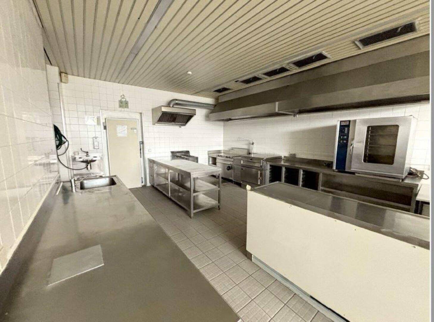 Professionelle Großküche mit umfangreichen Edelstahl-Arbeitsflächen, Geräten und gefliesten Böden.