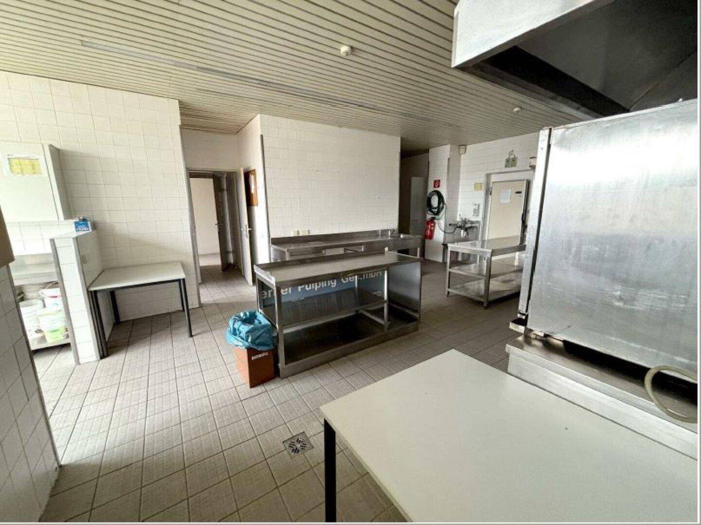 Weitläufige Großküche mit gefliesten Wänden, Edelstahlmöbeln und einem funktionalen Layout.