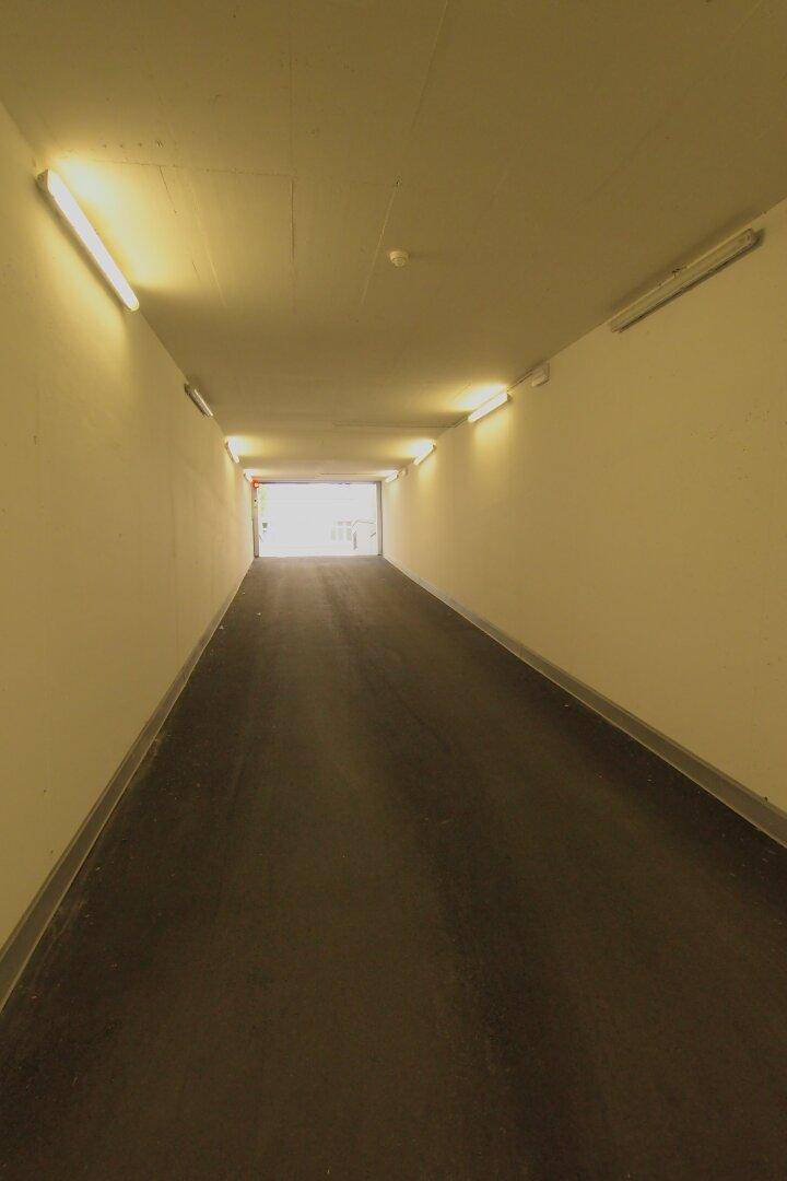 Heller und sauberer Zugangstunnel zur Tiefgarage mit seitlicher Beleuchtung und asphaltiertem Boden.