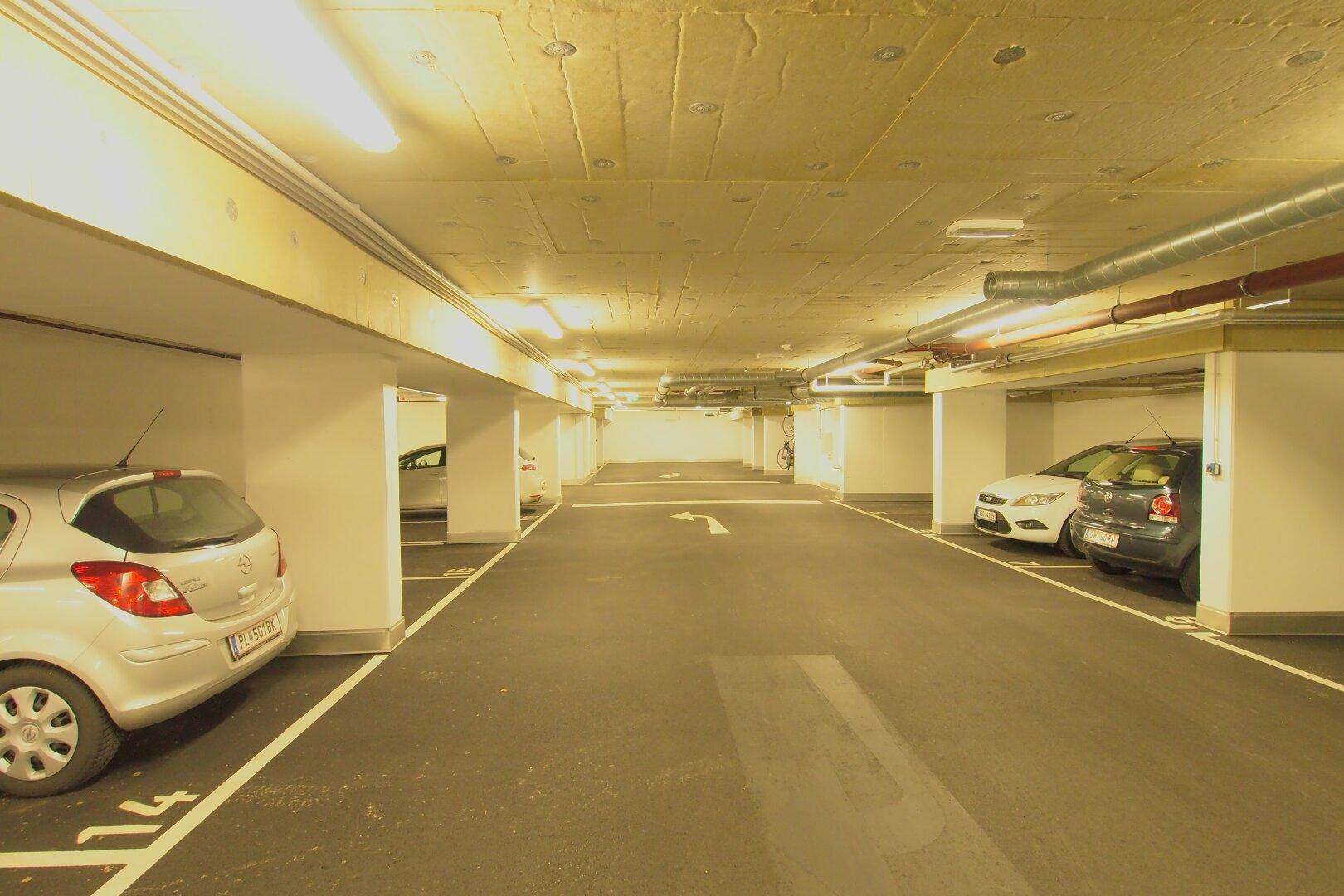 Geräumige und gut beleuchtete Tiefgarage mit markierten Stellplätzen und geparkten Fahrzeugen.