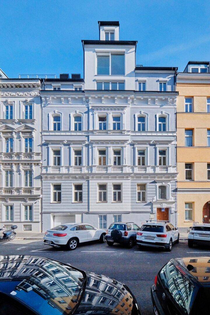 Historisches Gebäude mit hellblauer Fassade, vielen Fenstern und geparkten Autos davor.
