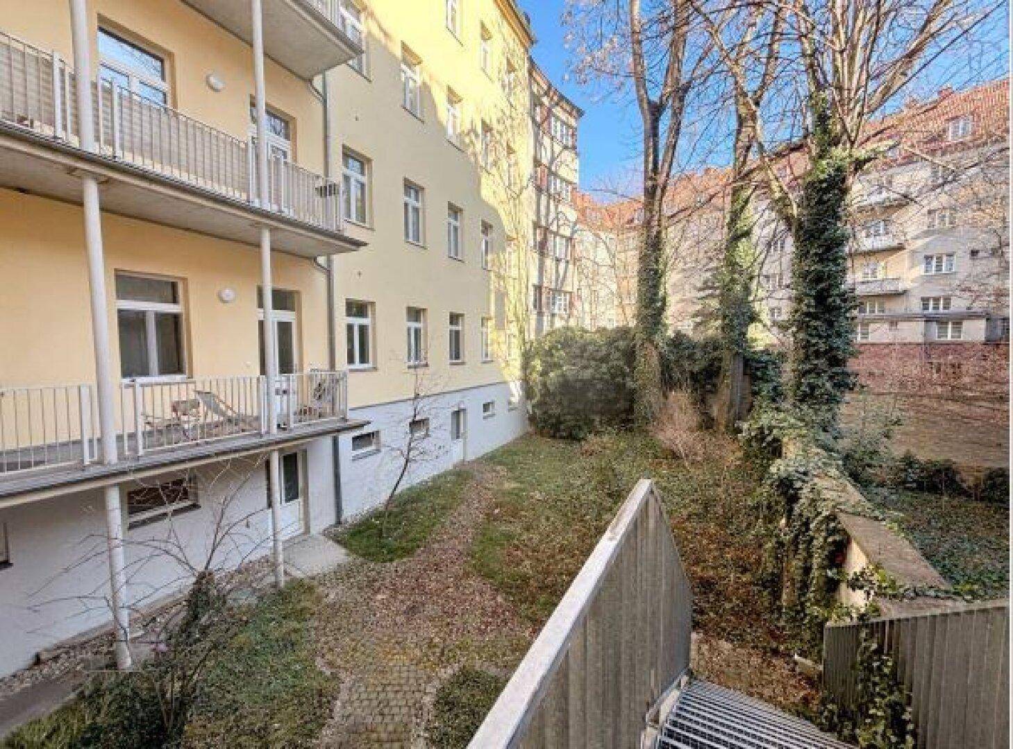 Hinterhofgarten mit Bäumen und Grünflächen, umgeben von Gebäuden, bietet eine ruhige Oase.