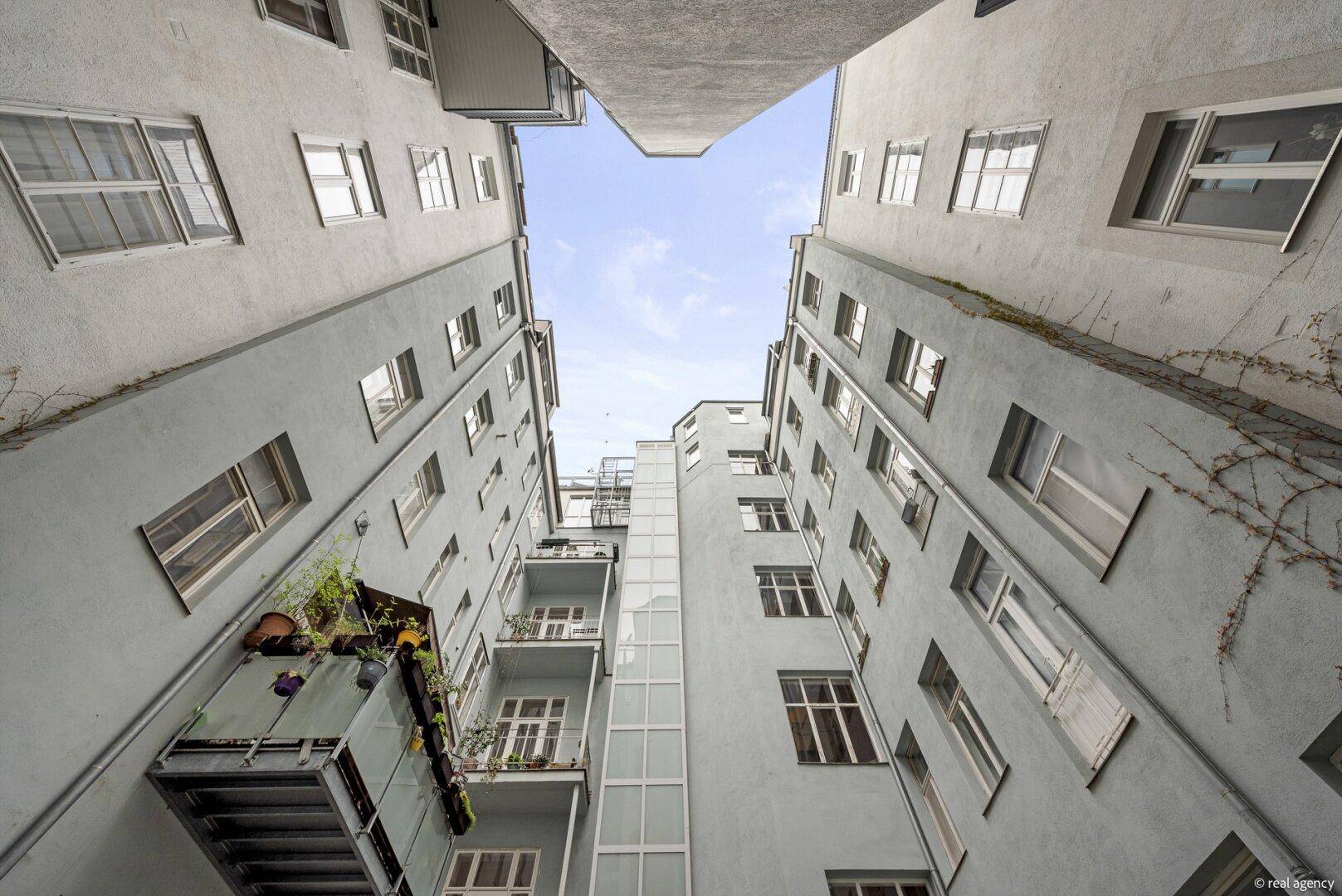 Innenhofansicht eines Mehrfamilienhauses mit mehreren Balkonen und einem externen Aufzug.
