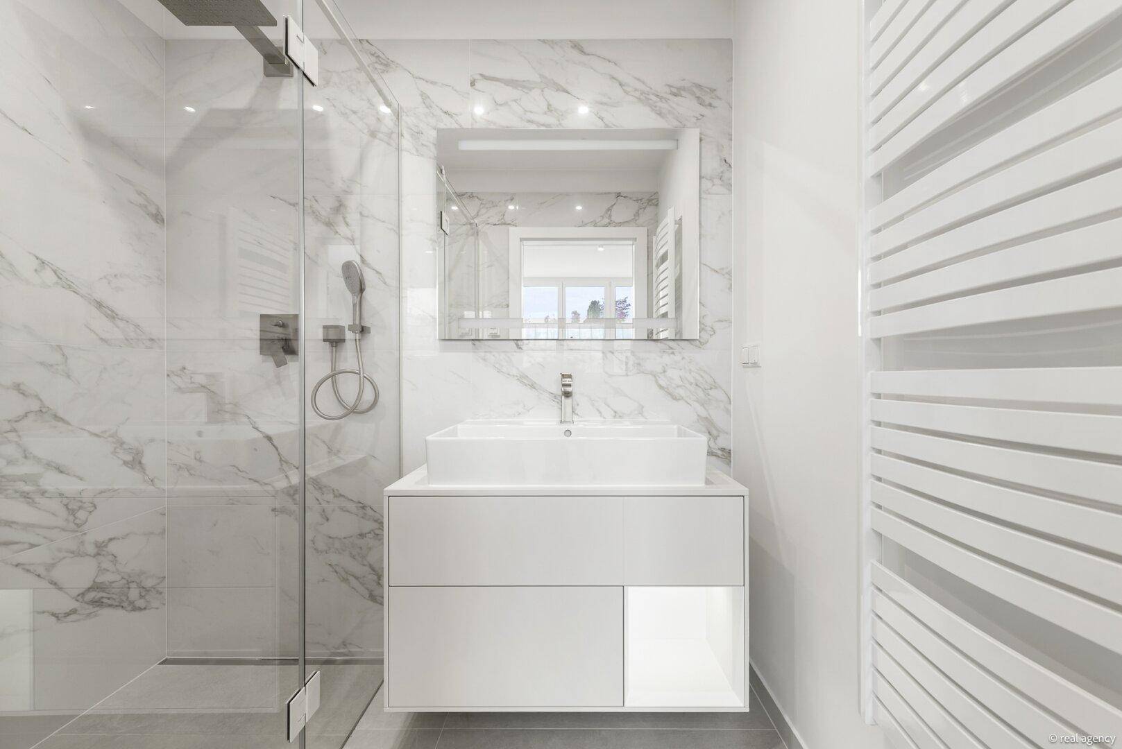 Modernes Badezimmer mit Marmorfliesen, begehbarer Dusche, Waschtisch und beheiztem Handtuchhalter.