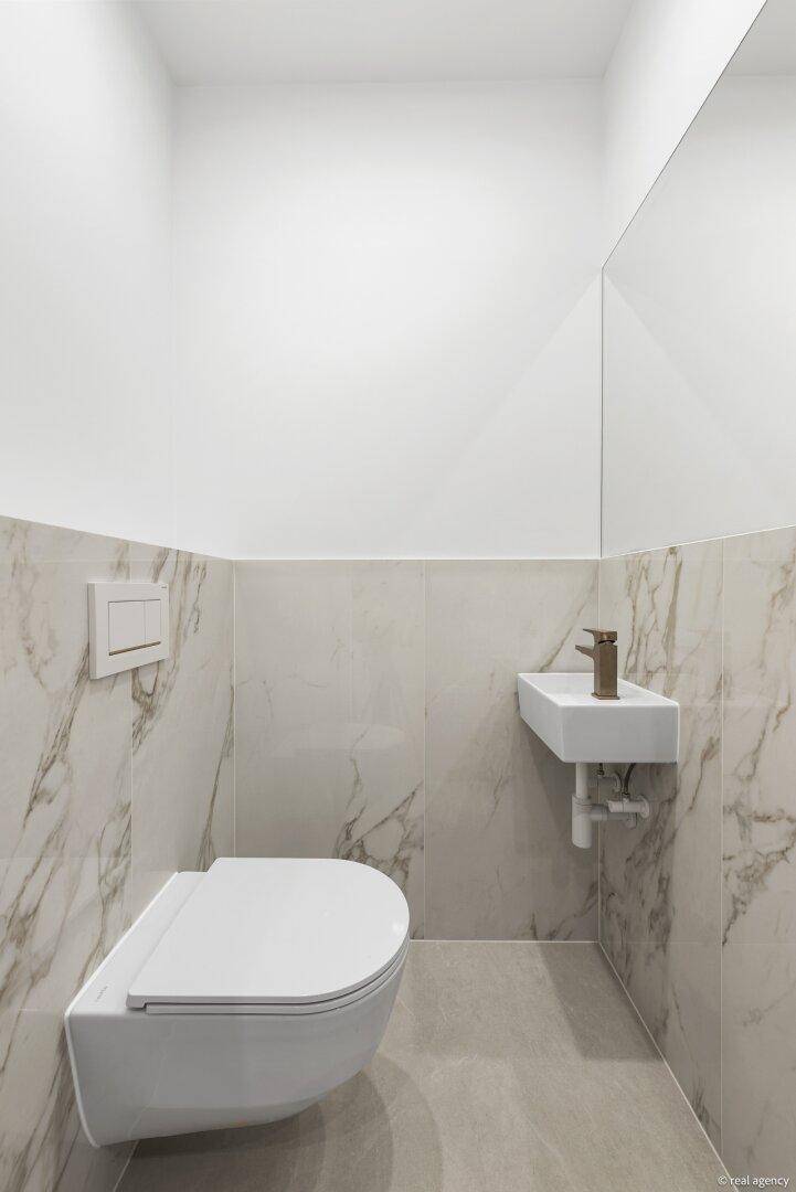 Elegantes Gäste-WC mit Wand-WC, kleinem Waschbecken und modernen Marmorfliesen an den Wänden.