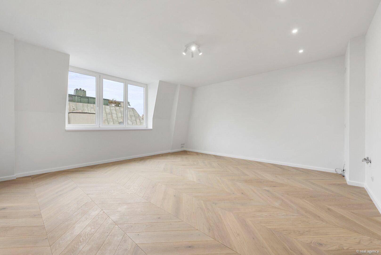 Heller Wohnraum mit elegantem Fischgrätparkett und großen Fenstern, die eine angenehme Atmosphäre schaffen.