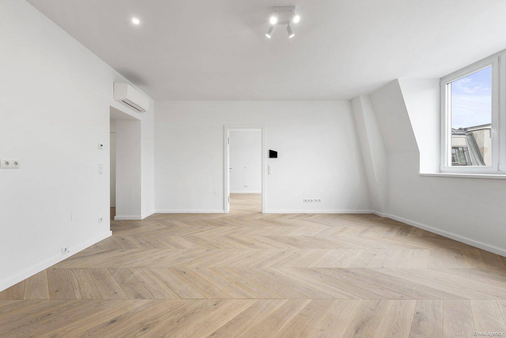 Lichtdurchfluteter Wohnraum mit Fischgrätparkett und Klimaanlage, der eine moderne und komfortable Umgebung bietet.