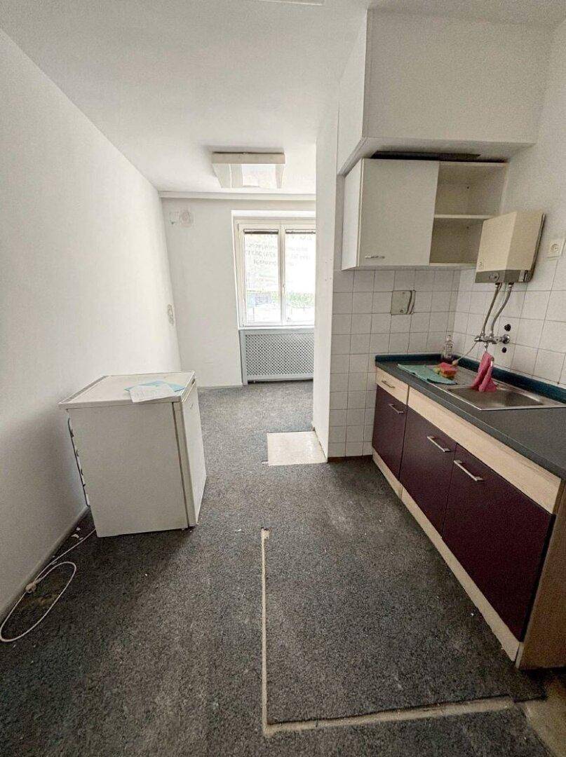 Eine einfache Küchenzeile mit Spüle, Unterschränken und einem Kühlschrank, ideal für eine kleine Büroküche.