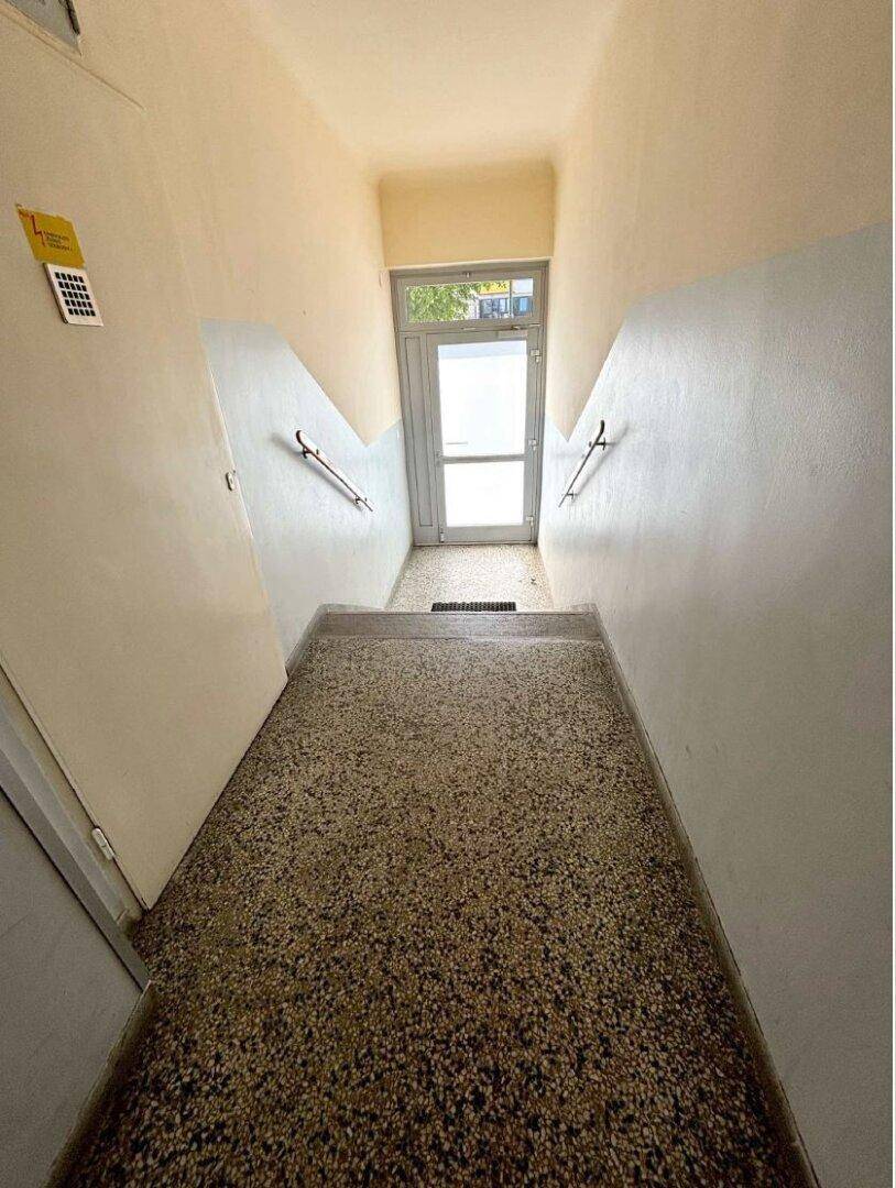 Ein heller Eingangsbereich mit Treppenabsatz, Handläufen und einer Glastür, die zum Außenbereich führt.