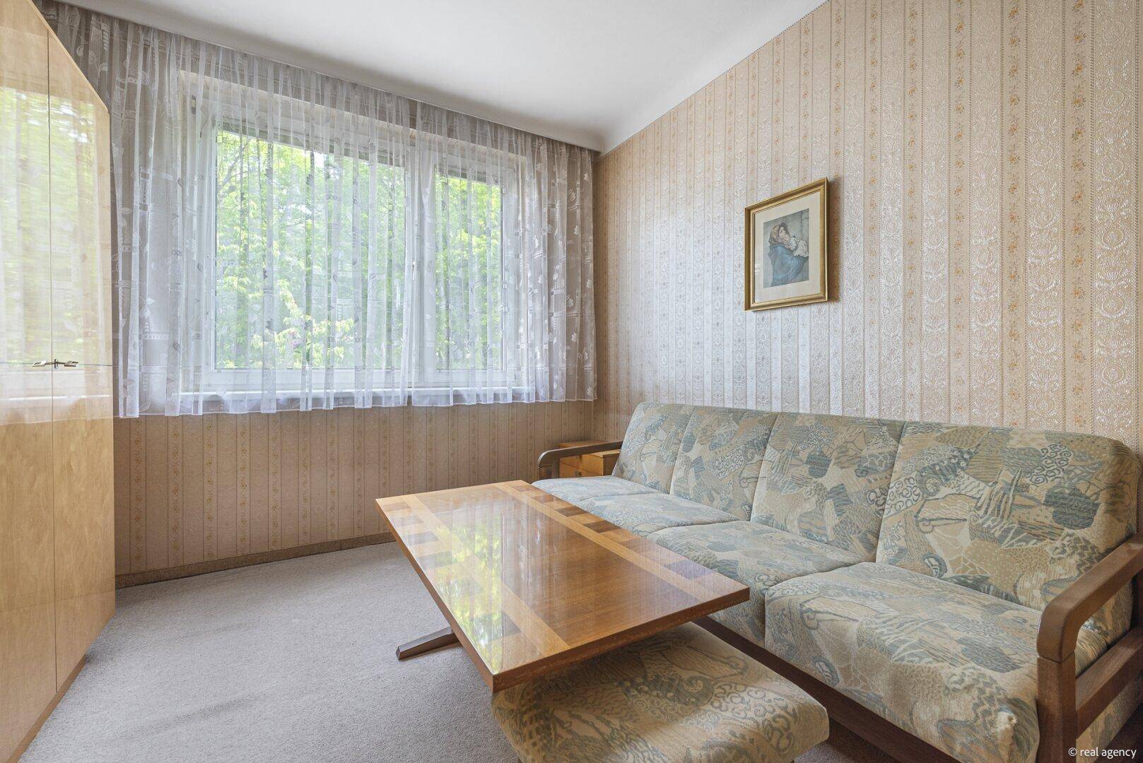 Gemütliches Zimmer mit Sofa, Couchtisch und großem Fenster mit Blick ins Grüne.
