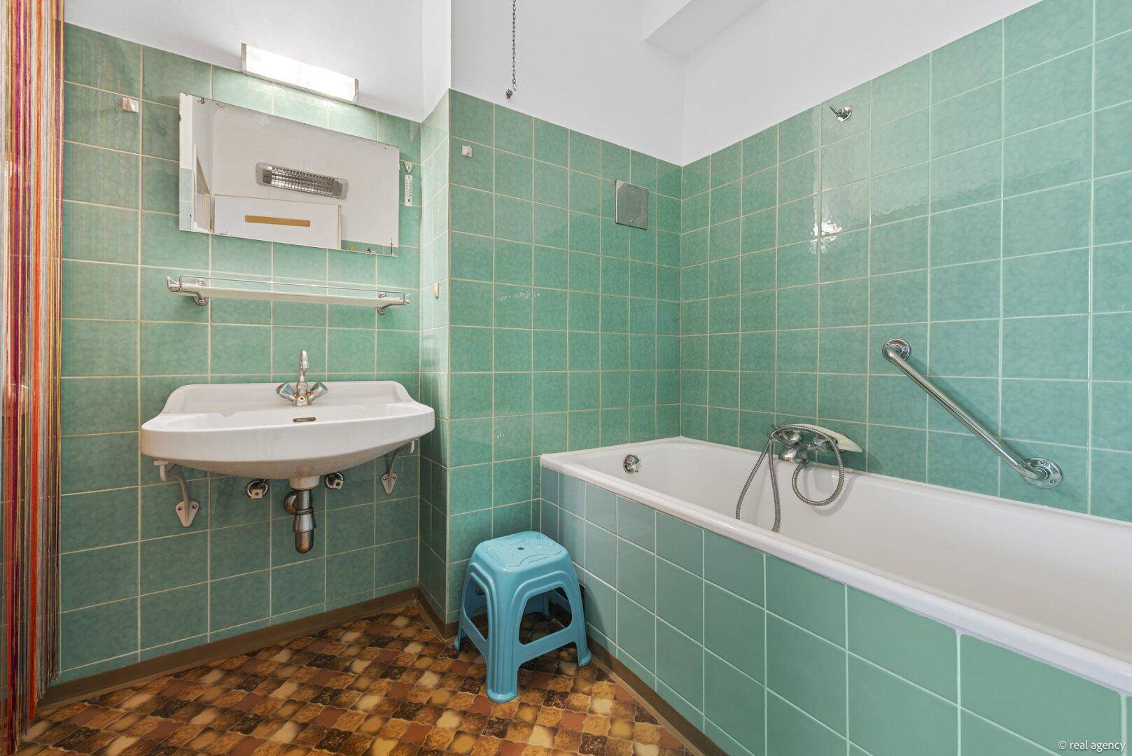 Badezimmer mit grünen Fliesen, Badewanne, Waschbecken und Haltegriffen für Barrierefreiheit.