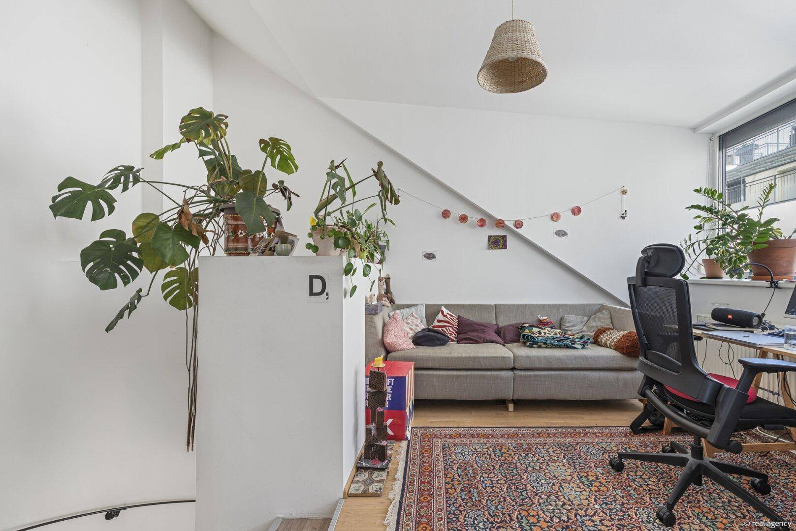 Heller Wohnbereich mit schrägen Wänden, Pflanzen und einem bequemen Sofa unter dem Dach.