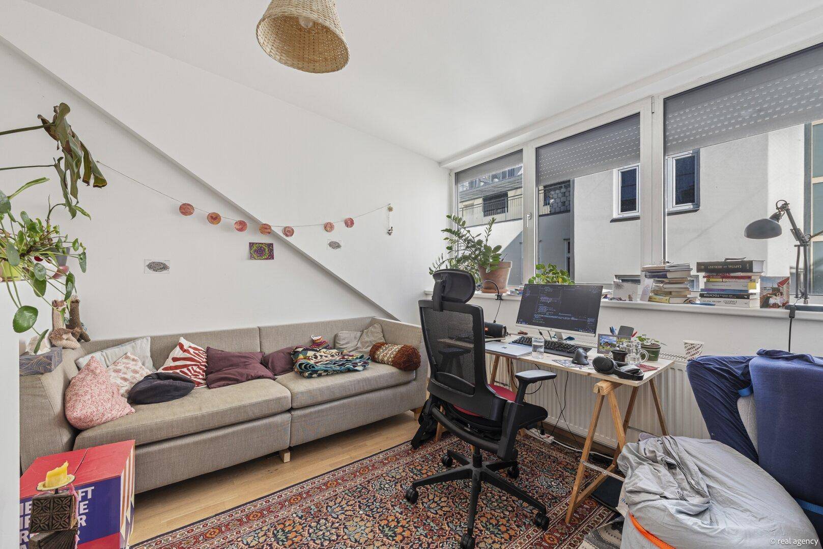Gemütliches Wohnzimmer mit Schreibtisch, Sofa und schrägen Wänden unter dem Dach.