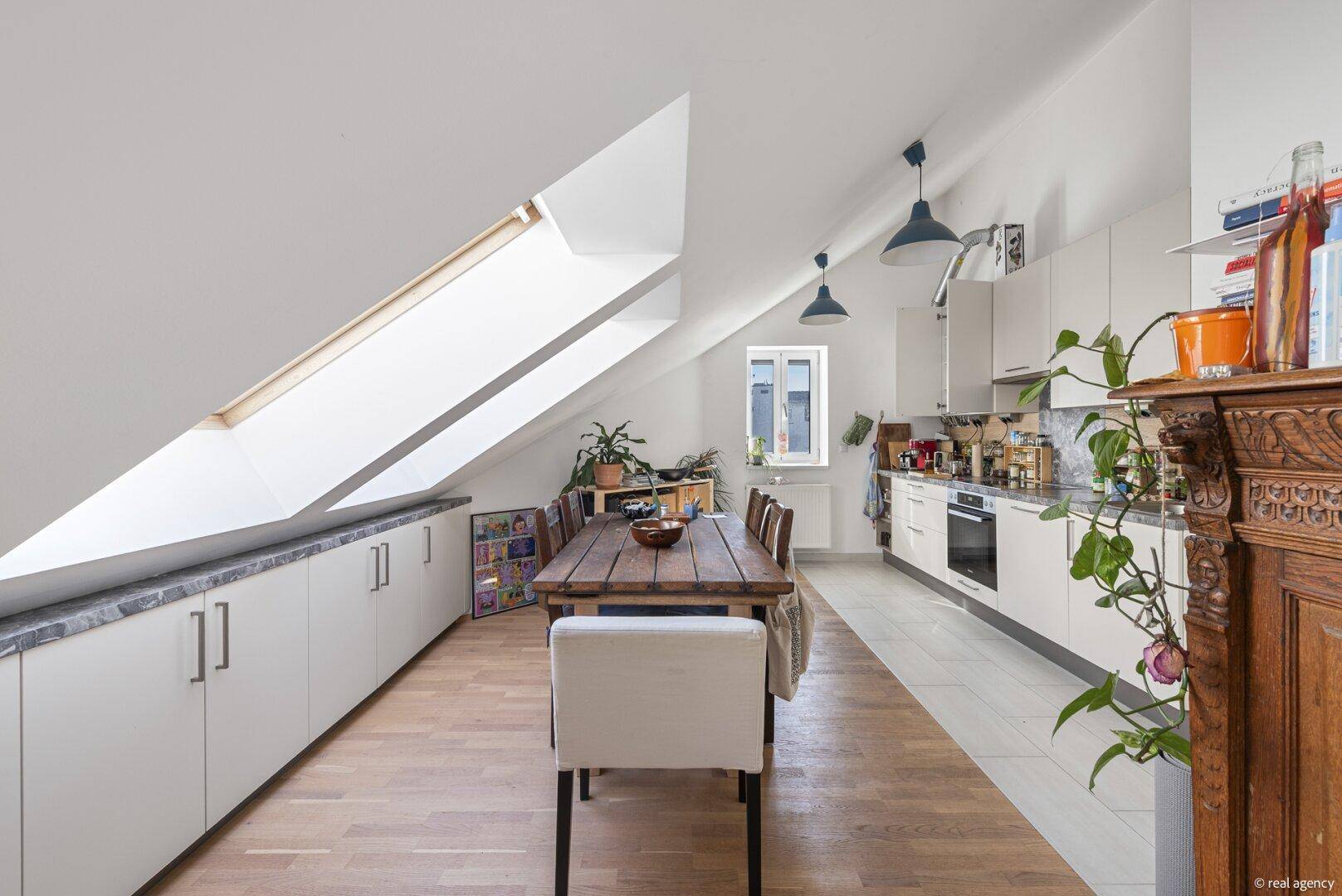 Offener Essbereich mit Holztisch und moderner Küche unter dem Dach mit Dachfenstern.