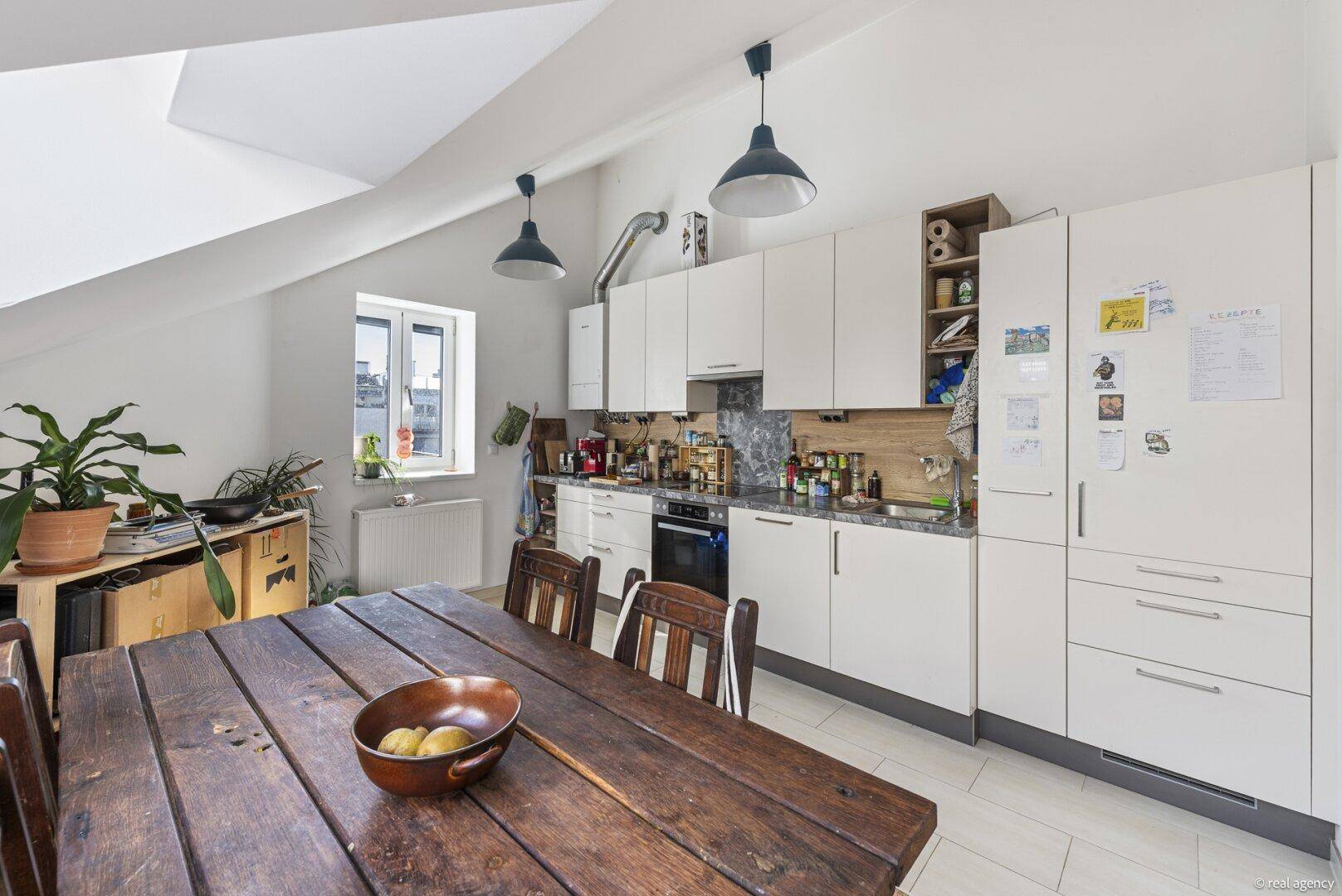 Moderne Einbauküche mit weißen Schränken, dunkler Arbeitsplatte und großem Esstisch.