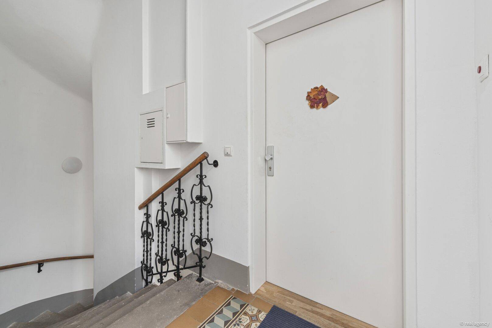 Eingangsbereich einer Wohnung mit weißer Tür und historischem Treppengeländer.