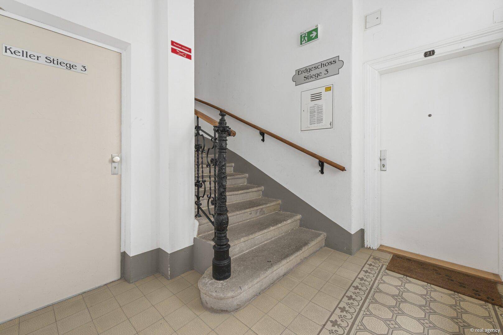 Heller Eingangsbereich im Erdgeschoss mit historischem Treppenhaus und Fliesenboden.