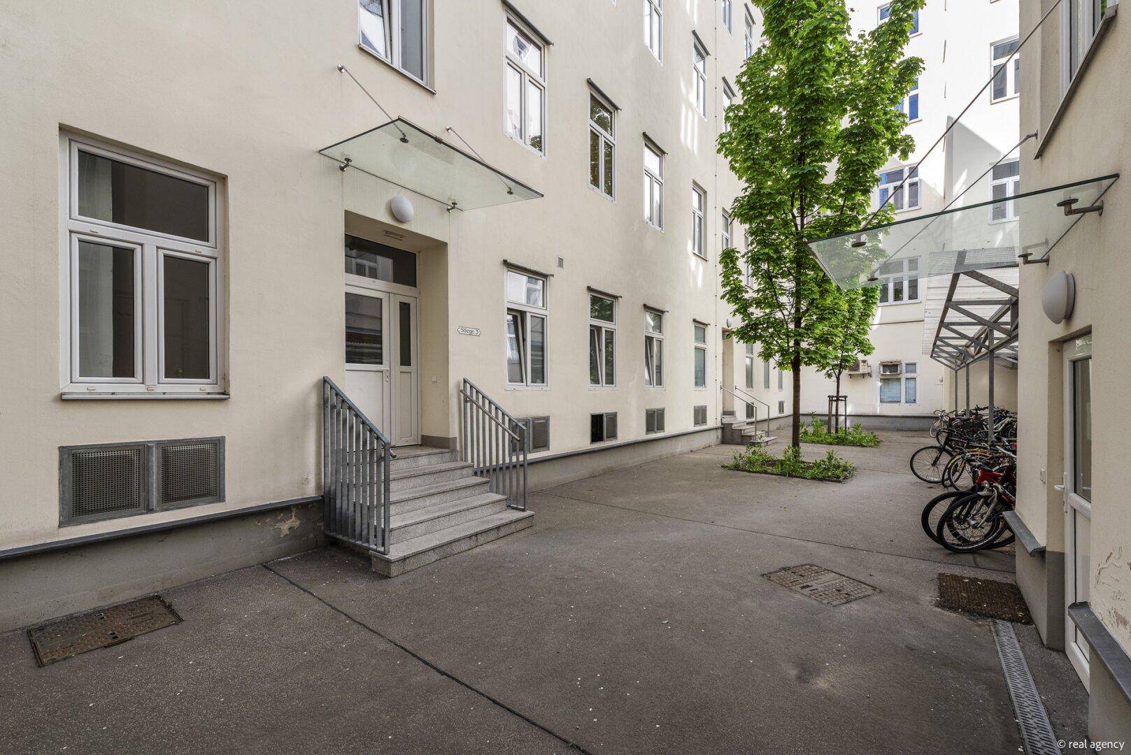 Eingangsbereich im Innenhof mit Baum und Zugang zu den Wohnungen.
