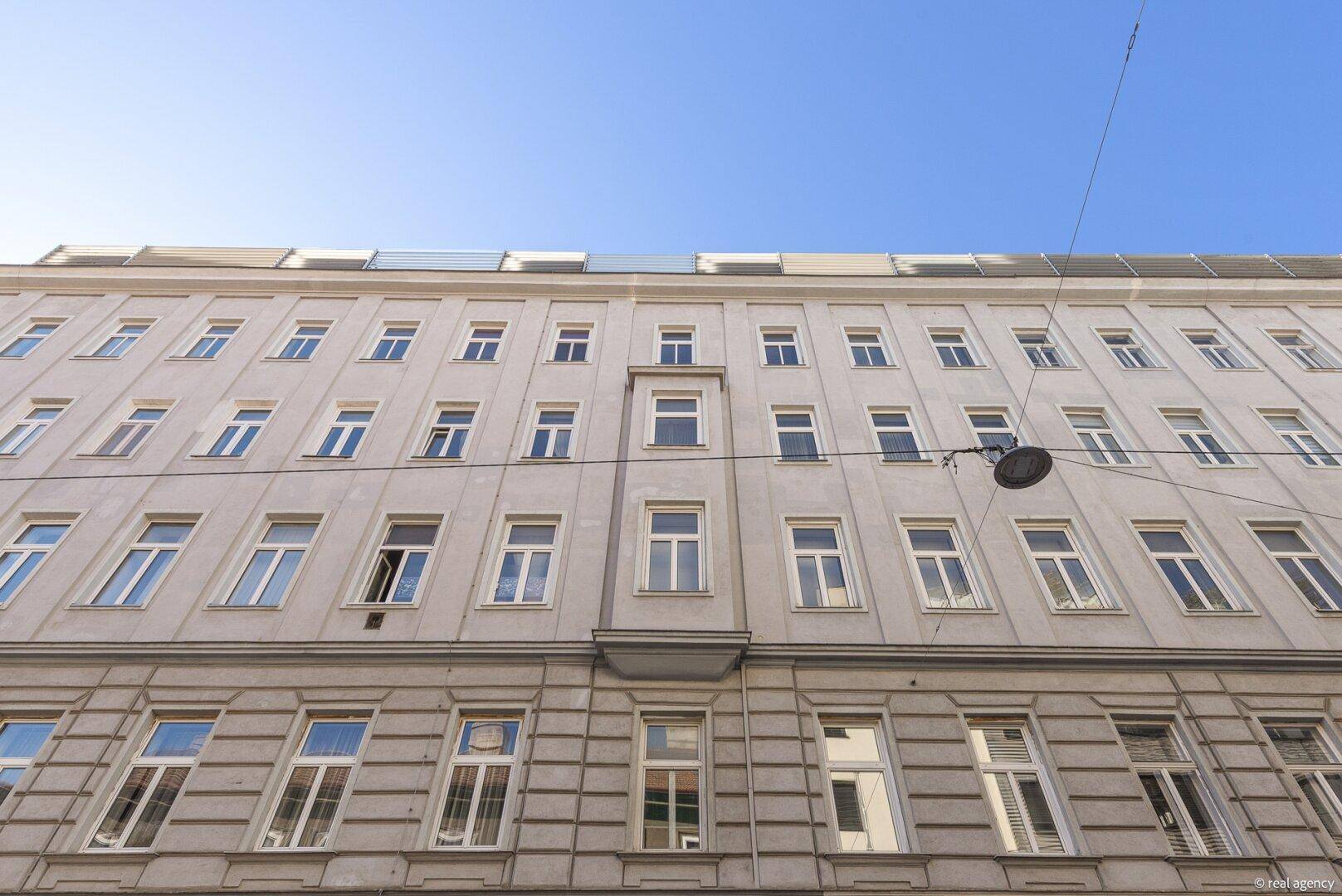 Klassische Fassade eines Altbaus mit vielen Fenstern unter blauem Himmel.