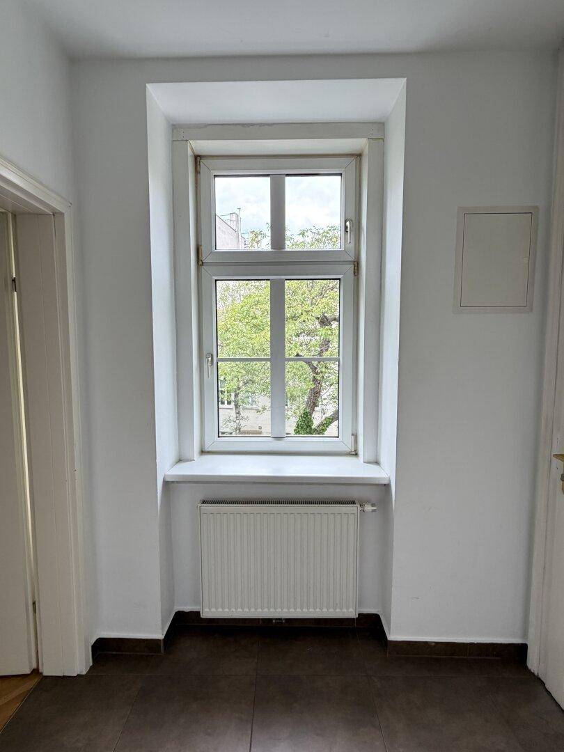 Heller Flur mit Fenster und Blick ins Grüne, ausgestattet mit einem Heizkörper.