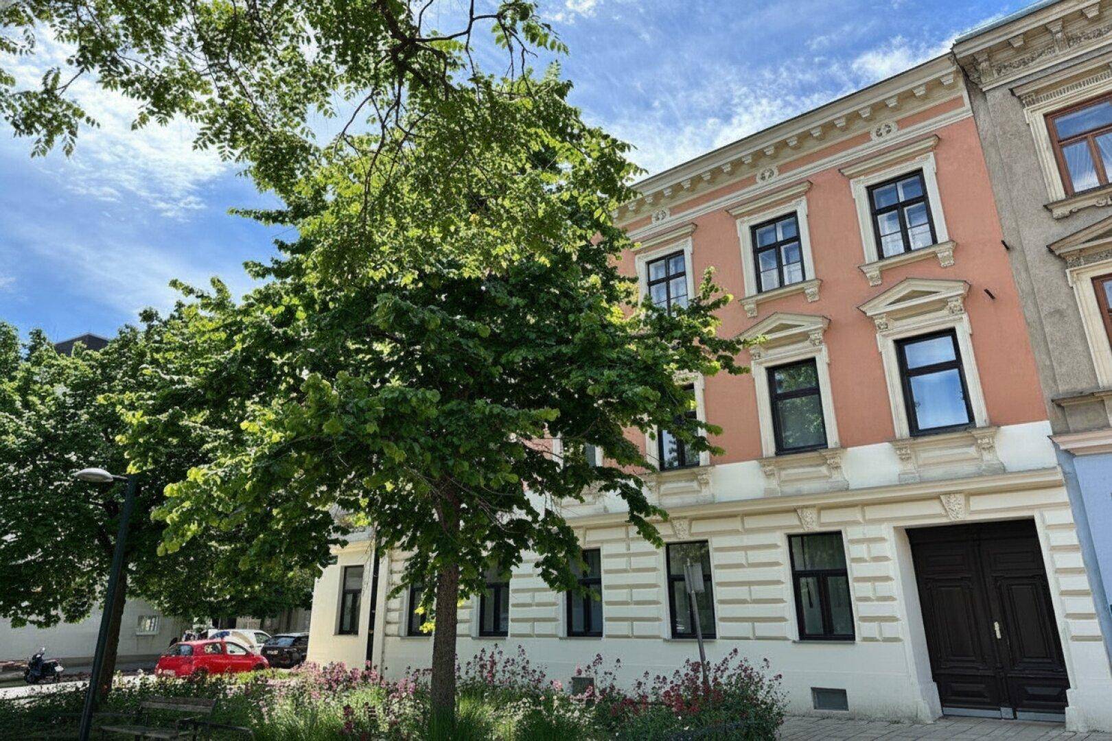 Attraktive Fassade eines Altbaus mit vielen Fenstern und grünen Bäumen davor.