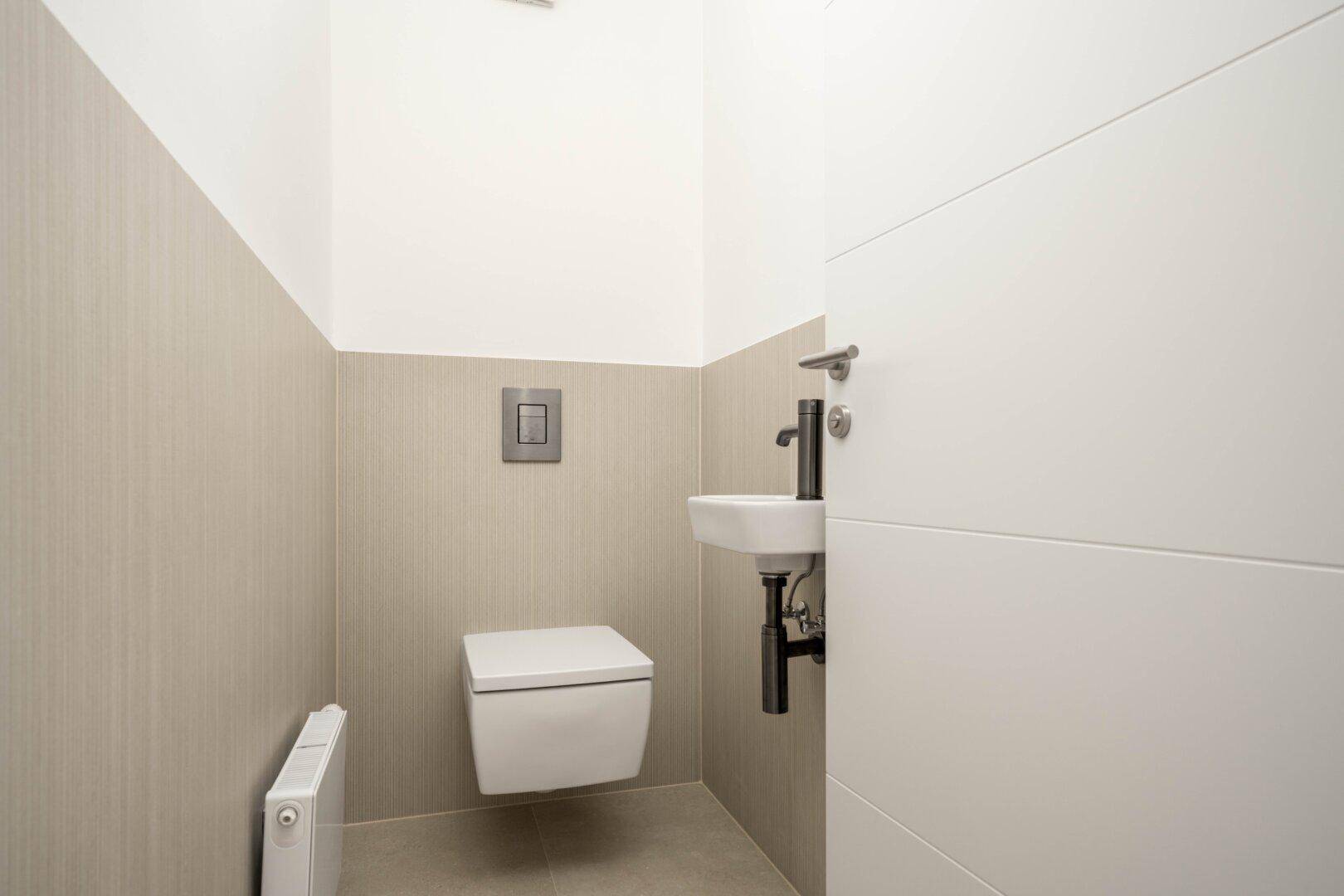 Modernes Gäste-WC mit wandhängender Toilette, kleinem Waschbecken und beigen Fliesen.